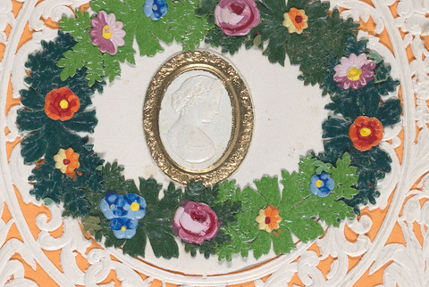Close-up of the cut-paper Valentine's card showing the center wreath of green leaves and colored flowers, and the cameo of the woman's face.