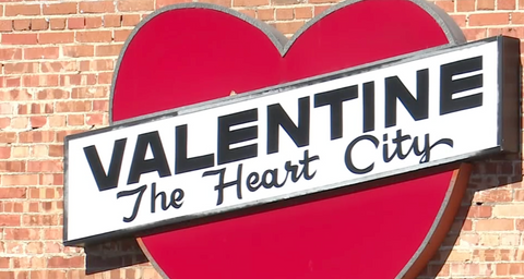 An exterior sign on a builing. The sign is shaped like a heart and reads, "VALENTINE, The Heart City."