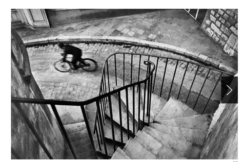 A bicyclist is riding along a street at the bottom of a windy staircase.