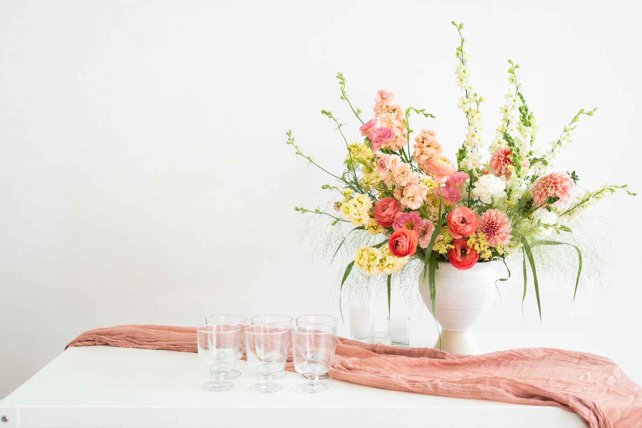 Tall Urn flower arrangement on a table with glassware and a pink sash