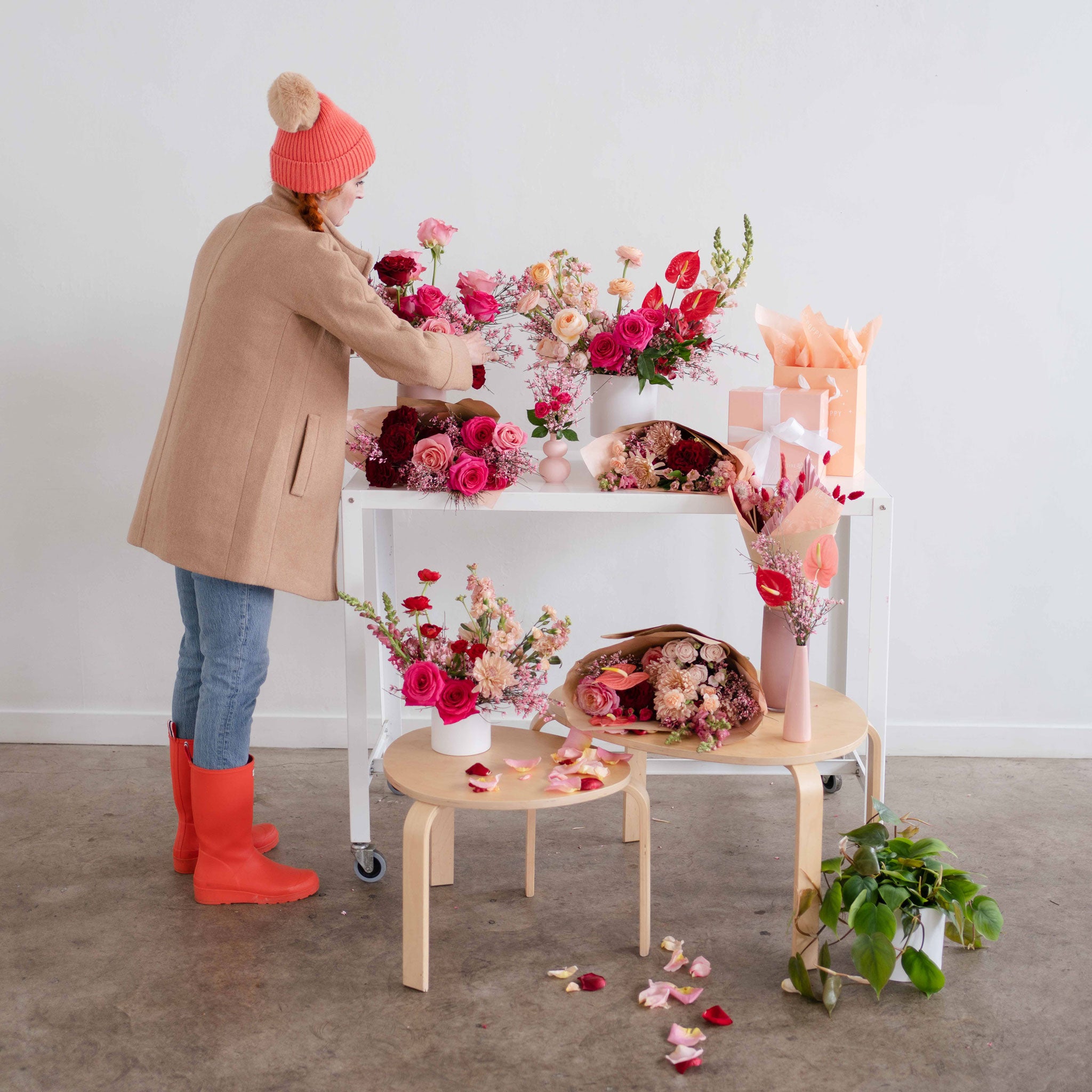 Woman styling flower arrangements wearing a beanie and rain boots