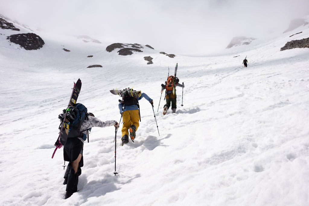 The Ring of Fire Group hikes up a snowy mountain with skis and snowboards on their backs.