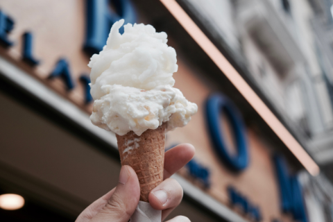 A person holding up a plain icecream cone in front of a store 