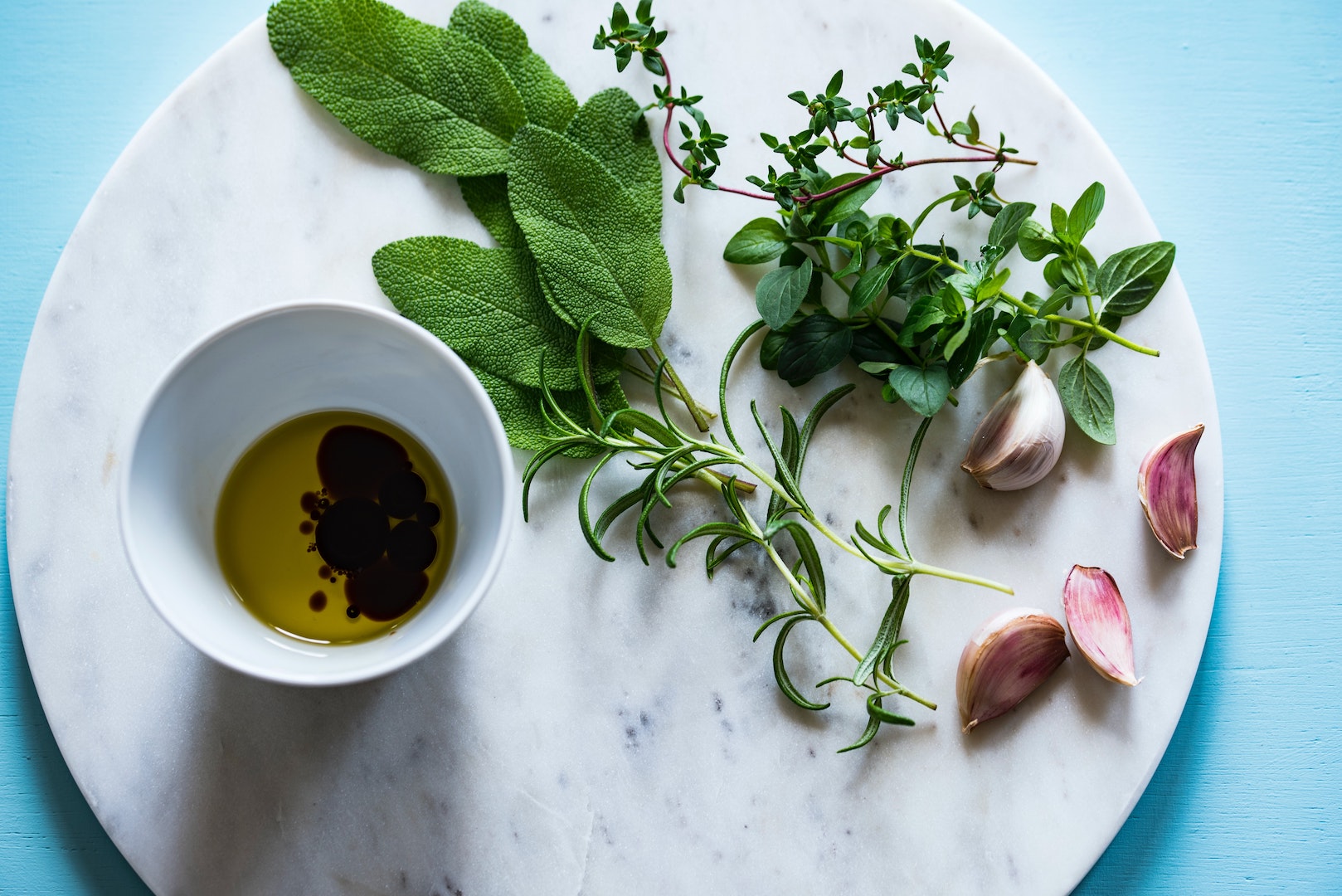 Image of LĒVO infused olive oil and vinegar next to the herbs used for an herbal infusion.