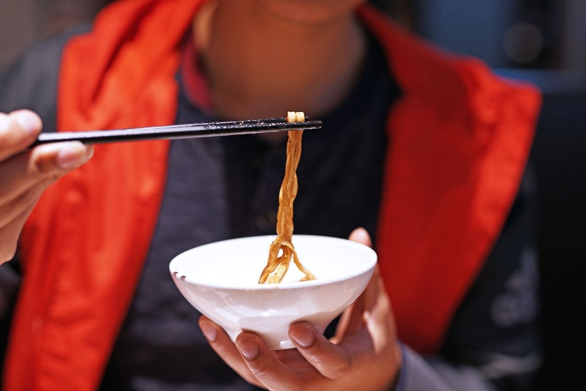 person in red vest eating soba noodles