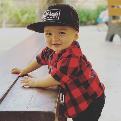 Cute kid in a long sleeve checkered shirt, wearing a kids trucker hat.