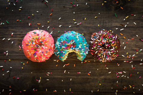 An image that shows three donuts sitting on top of a dark wood background. A bite has been taken out of the middle donut.