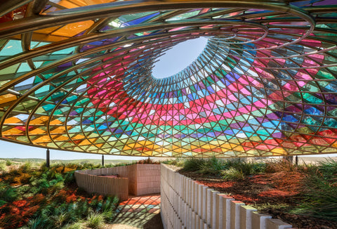 An image of what looks like a multi-colored glass gazebo sitting over top of an area with green vegetation and man-made seating areas.
