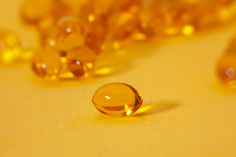 An image of several Vitamin D capsules on a yellow background.