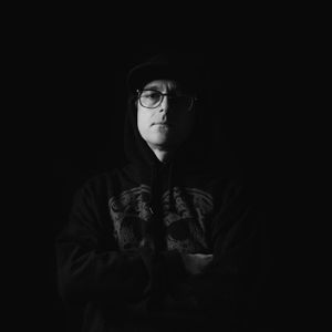 An image of Deadaelus in shadows, a white man wearing a black hoodie.