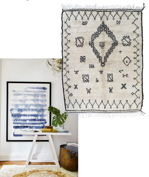 a small white desk sits on an antique rug with a large piece of abstract art behind it 