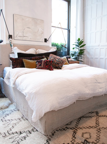 a large Moroccan berber rug styled beneath a large bed with cushy white linen bedding