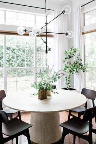 a circular dining table surrounded by floor to ceiling windows and lots of greenery