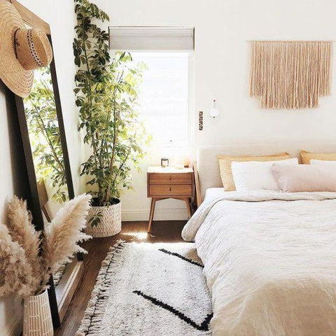 a bright, boho themed bedroom with a macramé wall hanging above the bed. A large Moroccan rug lies beneath the bed with a large mirror propped against the wall beside it