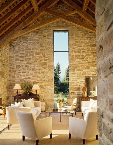 modern farmhouse with high, light stone walls and a tall skinny window.