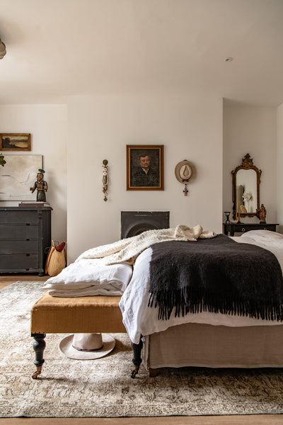 the guest bedroom with a large neutral-toned antique rug, and a bed with neutral and black bedding on top.