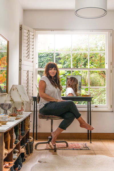 Heather sits in her walk in wardrobe/closet. A large window is visible behind her, with luscious greenery and flowers on view.