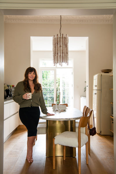 Heather standing beside a marble dining table with brass base. Behind is a pair of french doors painted white