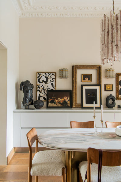 a wall of artworks, antique gold frames and wooden bowls, styled on top of a built in kitchen drawers.