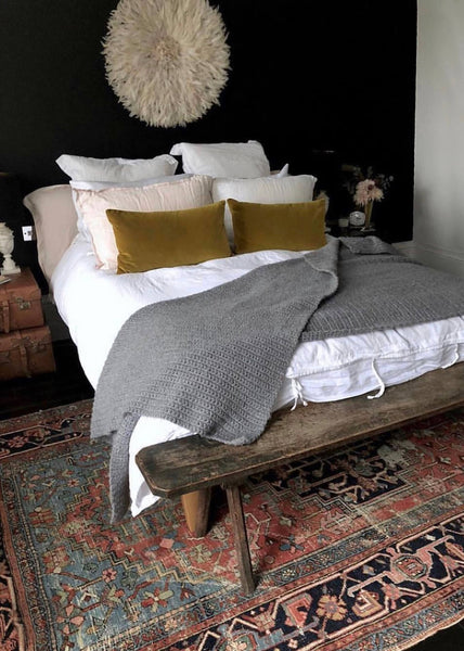 a colorful large Heriz rug beneath a large bed, with an antique wooden bench beside it.