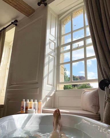 relaxing in a roll top bath while looking up at a Victorian window with light streaming through