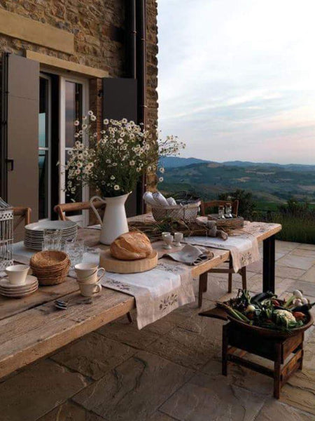 country patio with large wooden table, wild flowers and pretty crockery