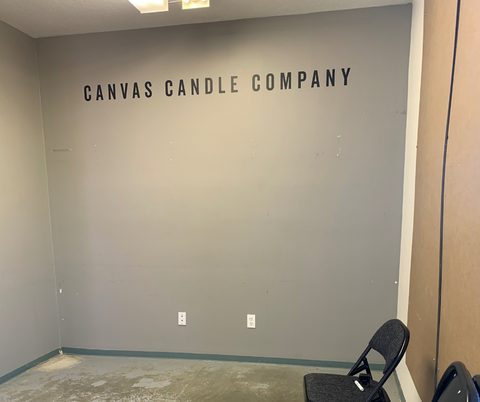 Empty room with black logo on wall "Canvas Candle Co"