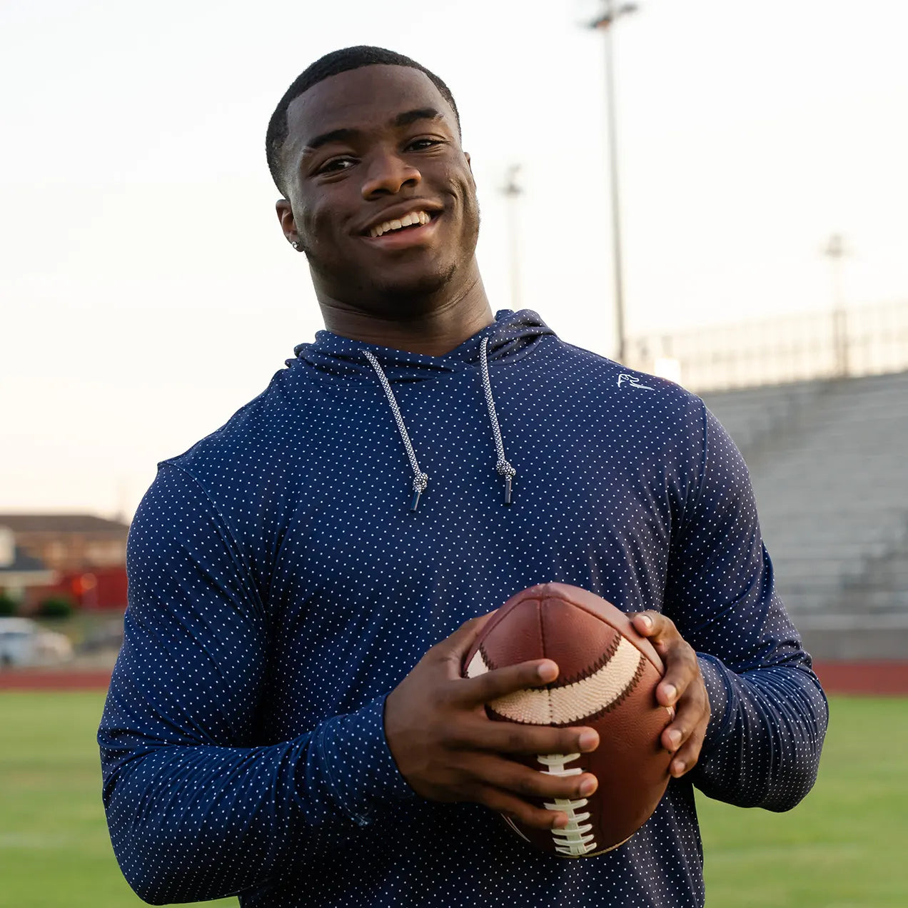 Jalen Milroe holding a football wearing The Capitol Hoodie