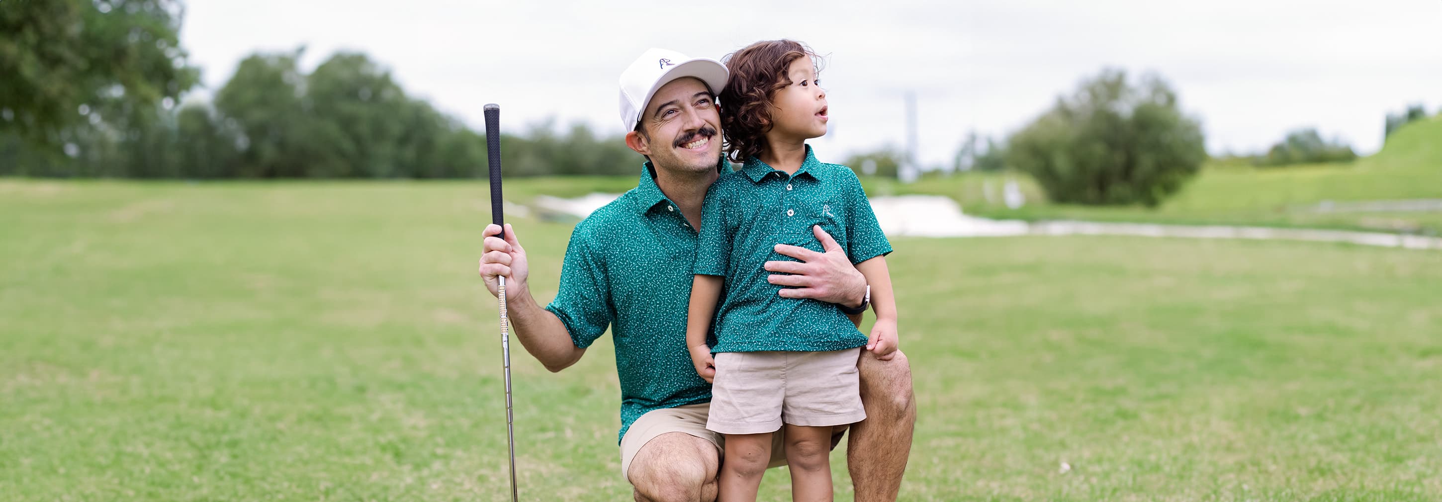 Dad hugging his son while holding a golf club and both wearing Rhoback Polos.