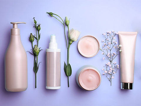 Pink bottles and jars of creams and lotions on lavender background