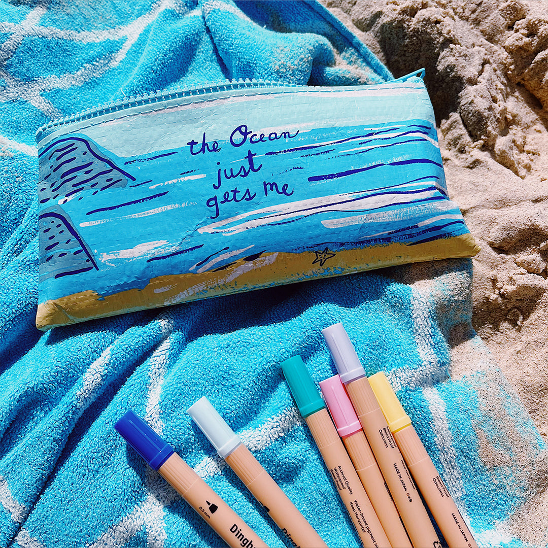 Eco-friendly Blue Q pencil case & Dingbats Atopens at the beach