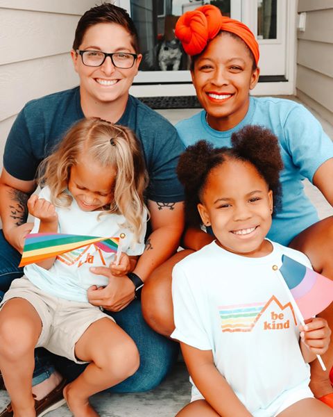 Family of two women and their two chilren with flags celebrating the right to vote. Click the photo credit link: abbyrollercoasterlife to be directed to the image shared on Instagram.