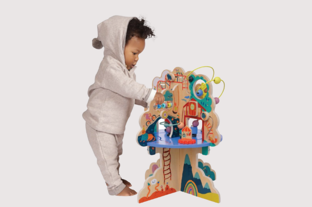 One year old boy standing next to wood activity center while playing. 