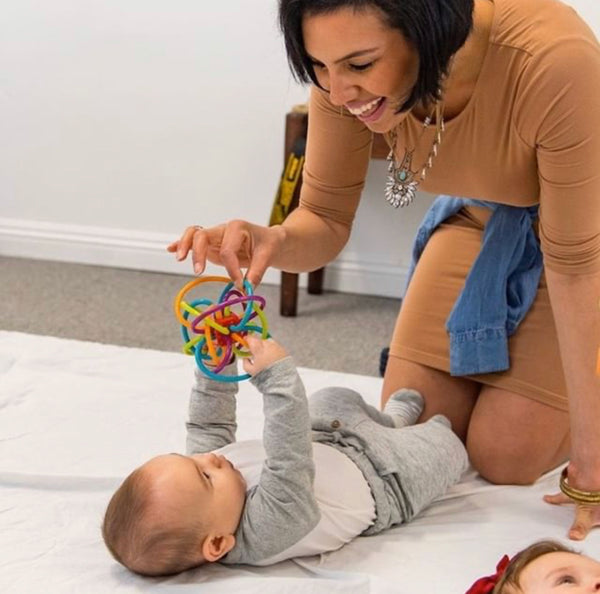 Mom shaking rattle toy in front of baby while baby is laying on a play mat. Photo credit to Instagram user @thefamilyroom