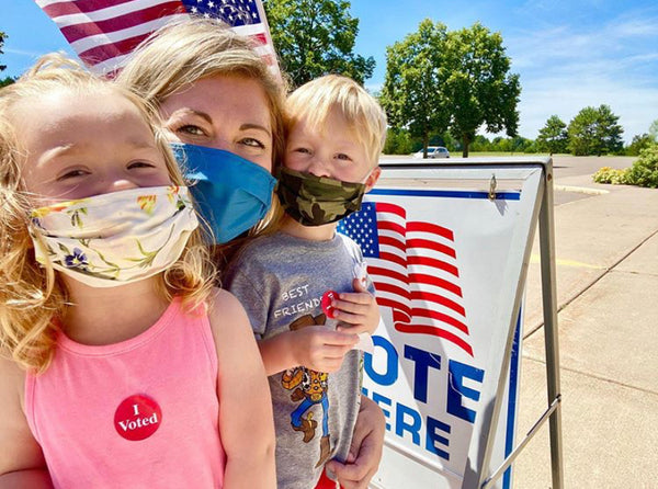 Mom and her two kids wearing facial masks, near a voter sign. Click the photo credit link: chels819 to visit the image shared on Instagram.