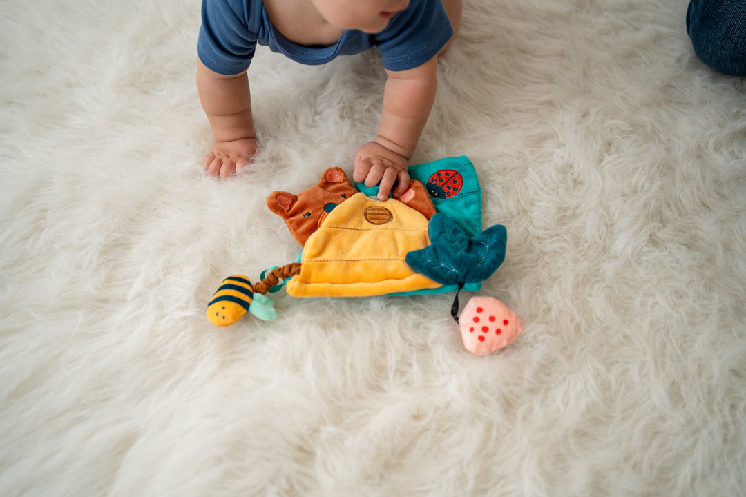 Baby on their knees reaching for a soft activity book