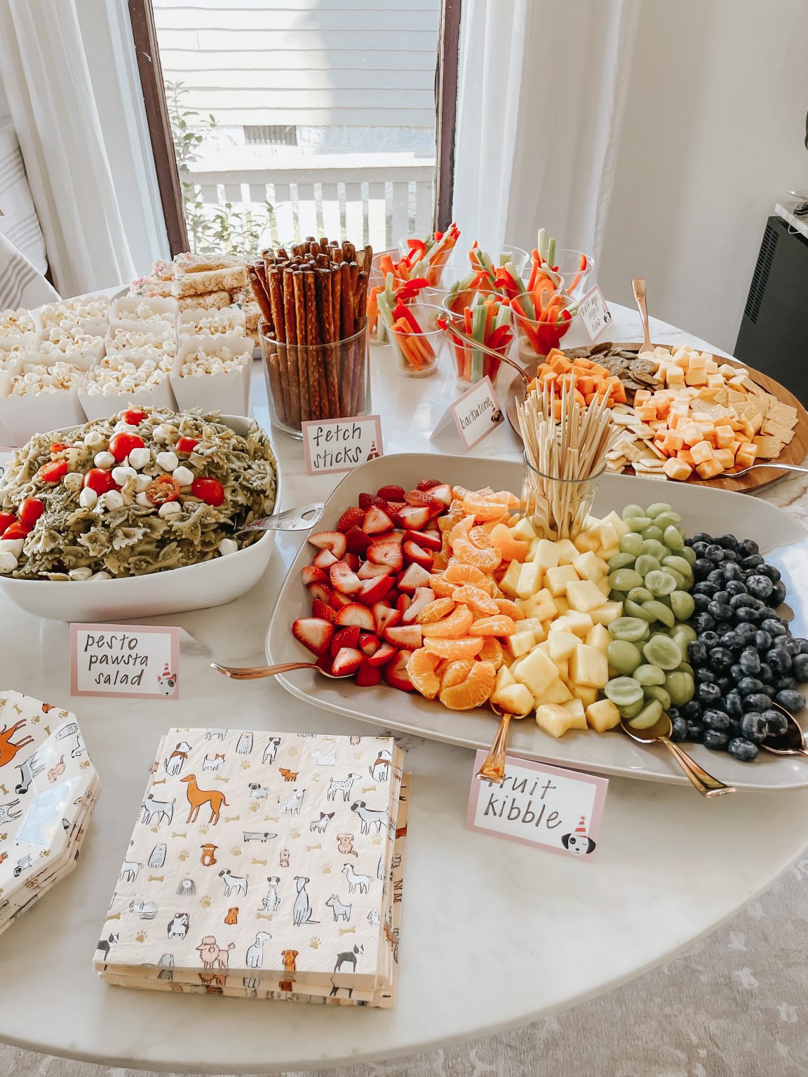 Foods on table related to puppy party theme including 'paw'sta salad, little cheese and veggie nibbles, pretzel sticks as fetch sticks. Photo credit to Lucky Andi.