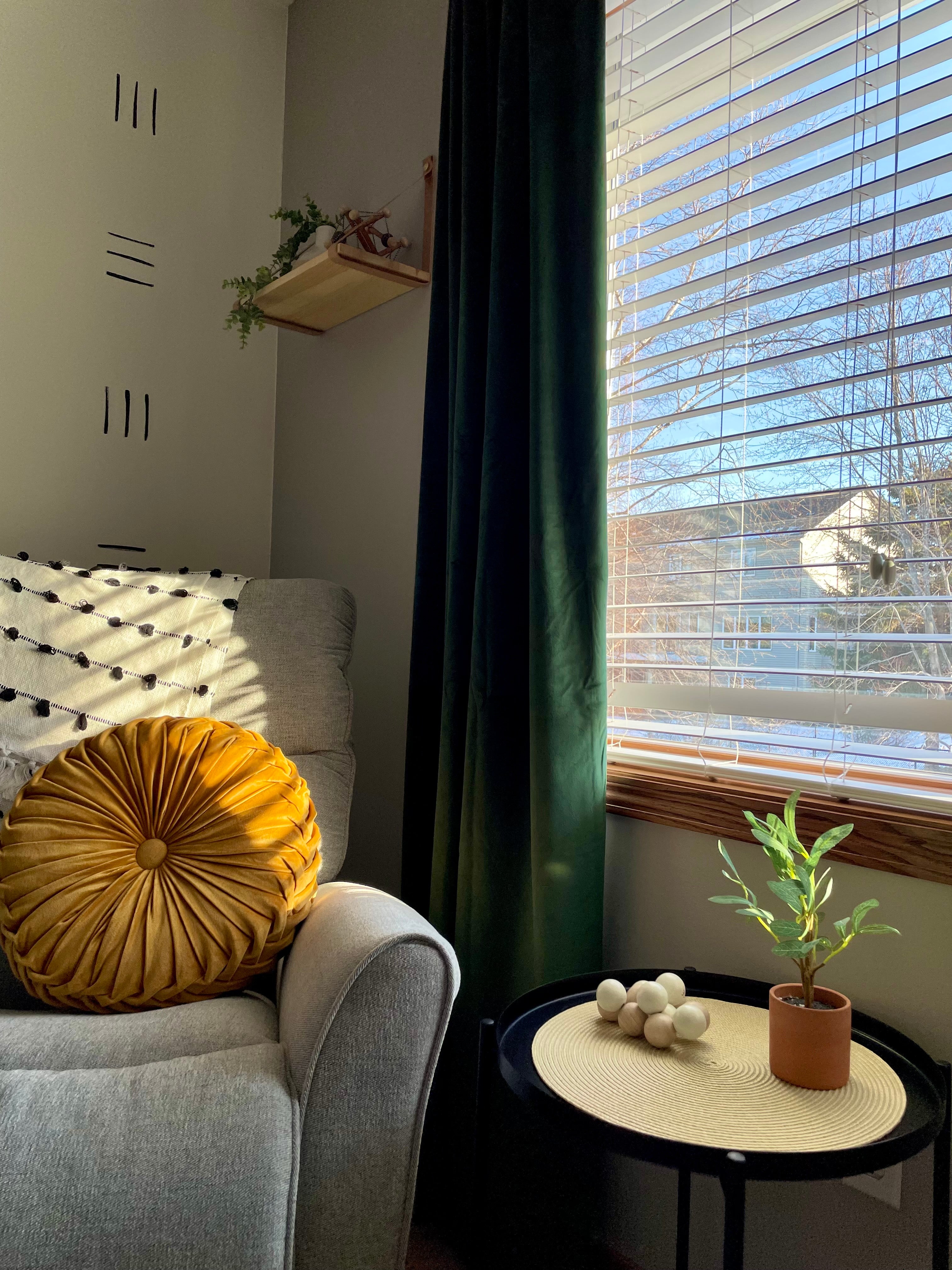 Room scene with velvet green drapes, rocking chair and side table with baby beads toy and plant.