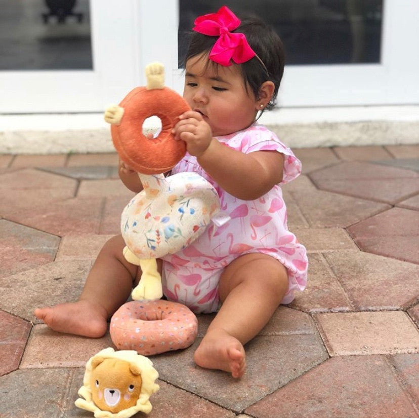 Latino baby girl seated on outside steps playing with the Safari Lion Plush Stacker toy. Photo credit to @emmaadelebf on Instagram.