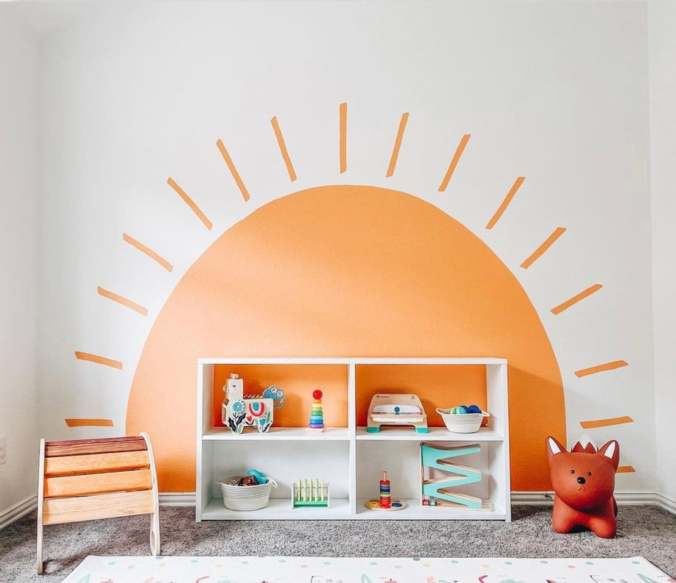 Play room scene with a bright orange sun on the wall, and a shelf full of toys from Manhattan Toy and other brands.
