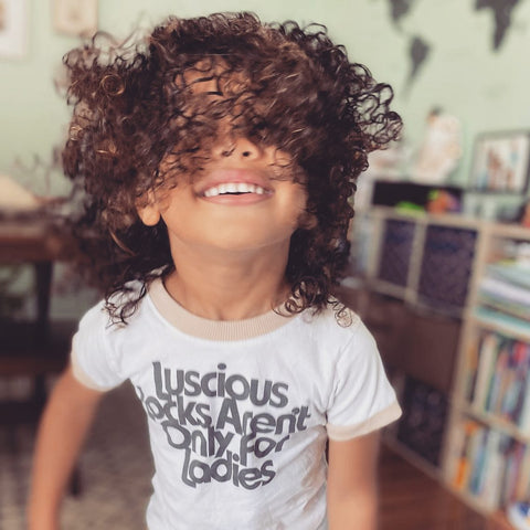 child with curly hair wears kids shirt that says "luscious locks aren't only for ladies"