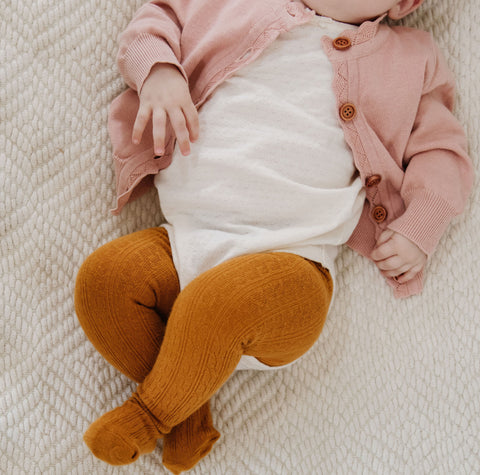 baby in onesie and mustard yellow cable knit tights