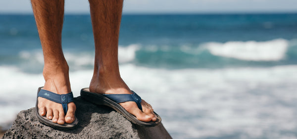 OluKai Ohana Sandals standing on a rock next to the ocean