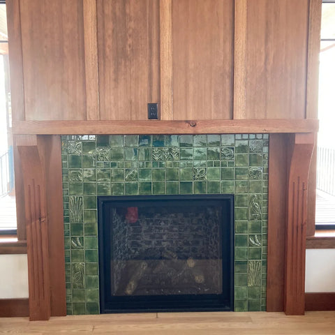 a fireplace tiled with green handmade tiles depicting plants and animals