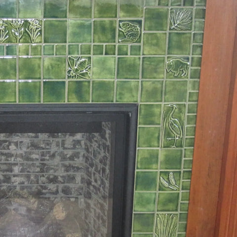 close up of green handmade tiles installed around a fireplace