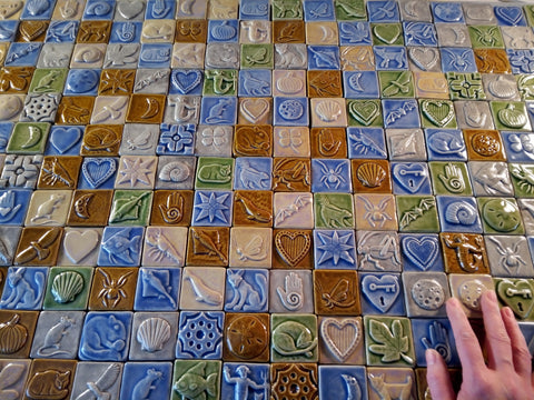 a large number of mult-colored handmade tiles laid out with the artist's hand in the lower right for scale