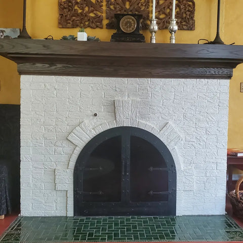 an arched brick fireplace painted white with a green handmade tiles on the floor in from