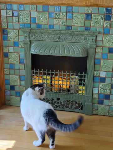 cat inspecting handmade tile hearth featuring animal and plant designs an green and blue colors