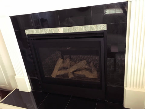small light colored handmade tiles depicting plants installed with black stone tiles in a fireplace surround