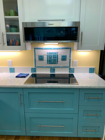 handmade turquoise sealife tiles installed amid white tiles in a kitchen with cupboards that match the handmade tiles